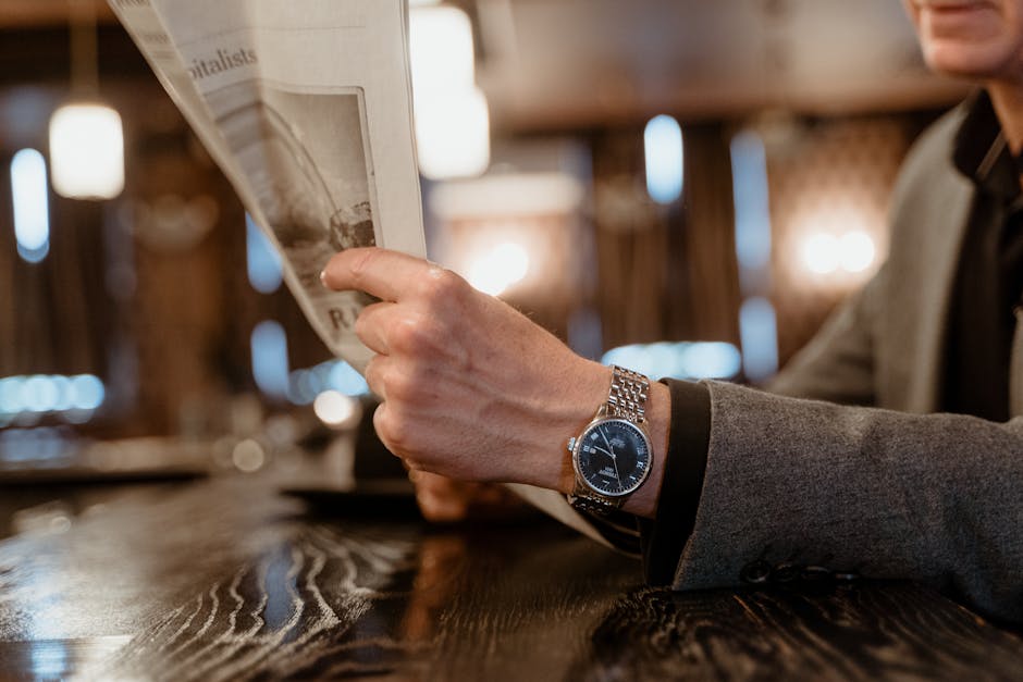 Close-up of a person's hand reading a newspaper in a cozy cafe, showcasing a classic wristwatch.
